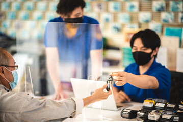 Young Asian sales man wearing covid-19 face protection mask while working on laptop giving car keys to senior customer during pandemic