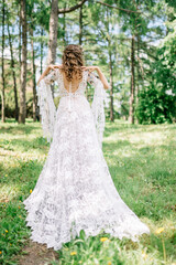 bride in a dress standing in a green garden and holding a wedding bouquet of flowers and greenery