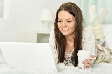 Young woman lying on bed with cup of coffee