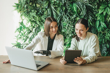 Two happy European women, one of them with disabilities, communicate, watch videos on a laptop,...