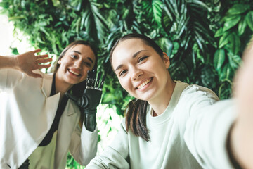 A happy European woman with a bionic prosthesis on her arm and her joyful friend take a selfie on...