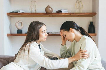 Obraz premium Two beautiful young European women, one with a bionic prosthesis on her arm, are sitting on the couch, experiencing stress, being depressed. Emotional support, burnout