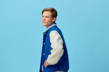 beautiful, happy an attractive young man student in a trendy bomber jacket and jeans stands on a blue background. Horizontal photo with empty space for advertising text