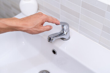 The faucet in the bathroom with running water. Man keeps turning off the water to save water energy...