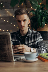 Serious young man browsing smartphone and looking at camera while working on freelance project remotely in cafe 