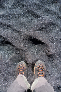 Legs in grey hinking trousers and black orange hiking boots on black sand