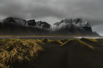Icelandic black-sand beach dune landscape with snow-powdered mountains in background, grey cloudy sky