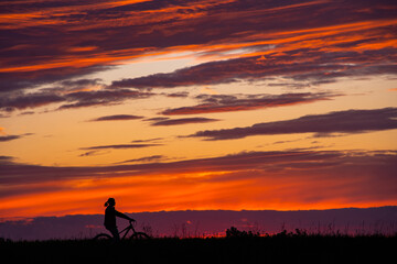 women riding bike at sunset. girls on a bike at beautiful sunset sky. silhouette of cyclist.