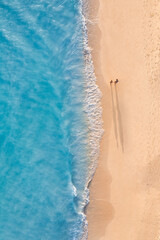 Aerial view of couple walking on beach with sunlight close to turquoise sea waves. Top view of...
