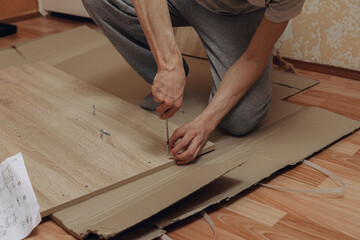 High angle of crop man assembling wooden furniture with screwdriver on floor at home  - Powered by Adobe