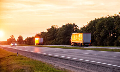 a convoy of trucks delivers cargo along the highway in the evening at sunset. The concept of cargo transportation and logistics companies FTL