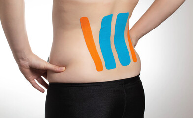 Kinesiological tape orange and blue on the back of the lumbar spine of the girl. Taping problem...