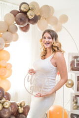 Pregnant woman holding "It's a Girl" sign, laughing, in front of balloon arch at her baby shower