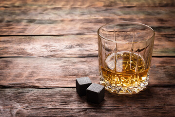 Whiskey in the drinking glass on the brown wooden table background.