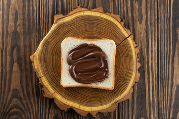 A slice of toast bread with chocolate paste on a wooden board. Horizontal orientation, top view.