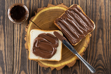 Slices of toast bread with chocolate paste and a knife on a wooden board. Horizontal orientation, top view.
