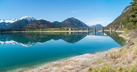 famous bridge across lake Sylvenstein, karwendel mountains reflecting in the clear water. view from the lakeside. bavarian landscape in spring