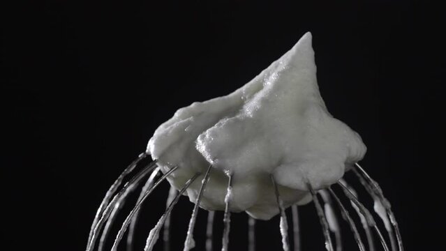 Metal whisk with whipped egg whites, isolated on black background, close up, rotates