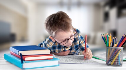 Kid boy doing homework at home, sitting at table with books and pen