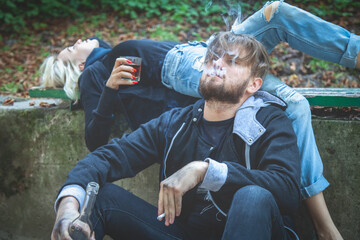 Couple of man and woman drinking vodka and smoking cigarette.  Drunk young people. Alcoholism, homelessness, social problem of dependence, destructive and antisocial behavior concept. - obrazy, fototapety, plakaty