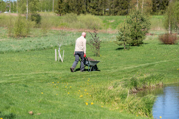 rear view of active senior man farmer pushing wheelbarrow in the field