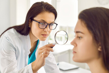 Woman gets professional skin exam at doctor's office. Dermatologist or cosmetology specialist uses...