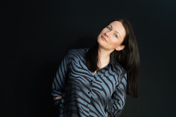 portrait of a flirtatious brunette with her hands behind her back over a black background
