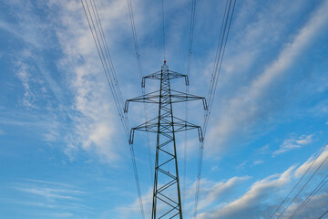 Large power lines metal carrier pylons in Europe. Low angle shot, cloudy blue sky background, no...
