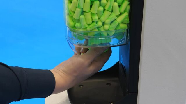 Male hand taking earplugs from ear plug dispenser by turning, blue background.