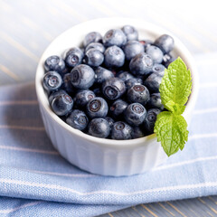 Forest blueberries with fresh mint leaf in white bowl on blue striped napkin close up.