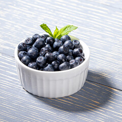 Forest blueberries with fresh mint leaf in white bowl on gray wooden table. Close up.