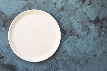 Empty white plate on blue concrete background. Top view, with copy space - obrazy, fototapety, plakaty