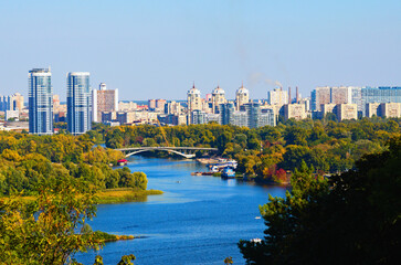 Obraz na płótnie Canvas Scenic autumn landscape view of Kyiv. Nature landscape with autumn colors. Dnipro River and Hydropark against blue sky. Modern colorful residential skyscrapers in the background. Kyiv, Ukraine