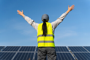 Fototapeta na wymiar Back view of the extremely happy excited woman wearing uniform widely opening hands and screaming feeling freedom while working at the solar panel farm