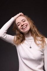 Happy young girl with long blond hair smiling. Young woman in white sweater pleased and satisfied. Portrait of  emotional lady isolated