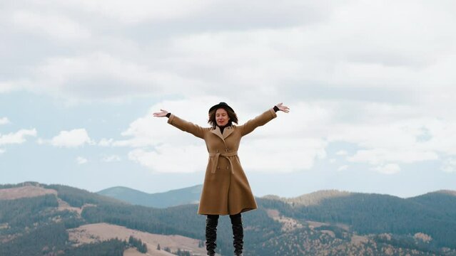 Girl stands against endless sky and admires nature and smiles. Woman feels freedom and raises hands up and breathes fresh mountain air. Female is filled with energy from nature. Calmness and serenity