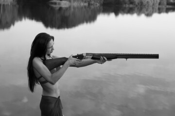 Beautiful woman with a shotgun at the lake in black and white