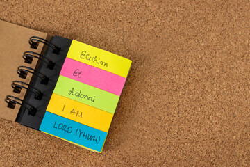 Names of God (Elohim, El, Adonai, I AM, LORD-YHWH) written on colorful note stickers on a textured background with copy space. Top view. Christian biblical concept, titles of God from Holy Bible Book.