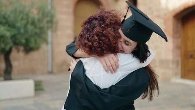 Two women mother and daughter hugging each other celebrating graduation at campus university