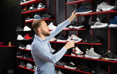 Man choosing sports shoes for running standing in the modern sportswear shop, shopper choosing...