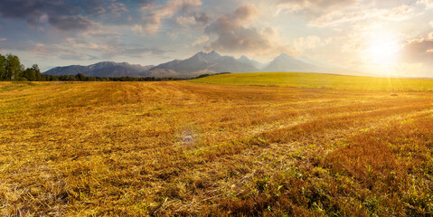 beautiful countryside landscape at sunset. idyllic rural scenery with, fields in summer in evening light. mountain ridge with high peaks in the distance. wonderful cloudscape on the sky