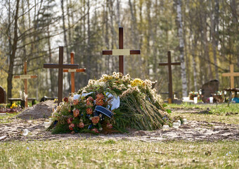 New grave with wooden cross and several funeral wreaths. Another graves with crosses behind it....
