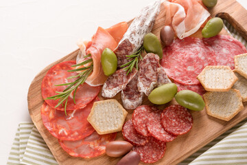 Traditional italian antipasti on white concrete table background. Wooden charcuterie board with different types of sausages - salami, bresaola, proscuitto served with olives and crackers