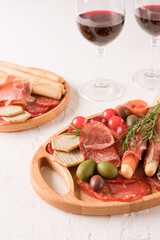 Charcuterie plate with different types of meat snacks - proscuitto. Wooden plates with traditional italian antipasti served with glasses of red wine on white concrete table. Vertical image
