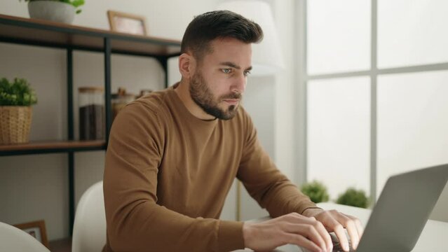 Young hispanic man using laptop sitting on table at home