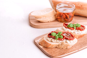 Fototapeta na wymiar Healthy breakfast ideas concept. Delicious toasts with ricotta cheese, sun dried tomatoes with olive oil on wooden cutting board over white table with copy space. Classic italian appetizer