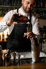 view of man bartender hands holding bottle and pours beverage into steel jigger