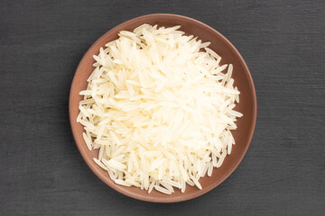 Long Basmati rice in clay plate on black wooden background. Macro. Flat lay. Indian cuisine concept