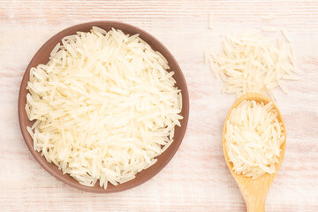 Long Basmati rice in clay plate spoon and bunch on brown wooden background. Macro. Flat lay. Indian cuisine concept