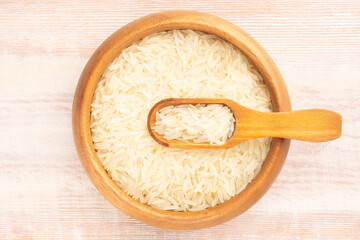 Long Basmati rice in wooden bowl and scoop on brown background. Macro. Flat lay. Healthy eating concept
